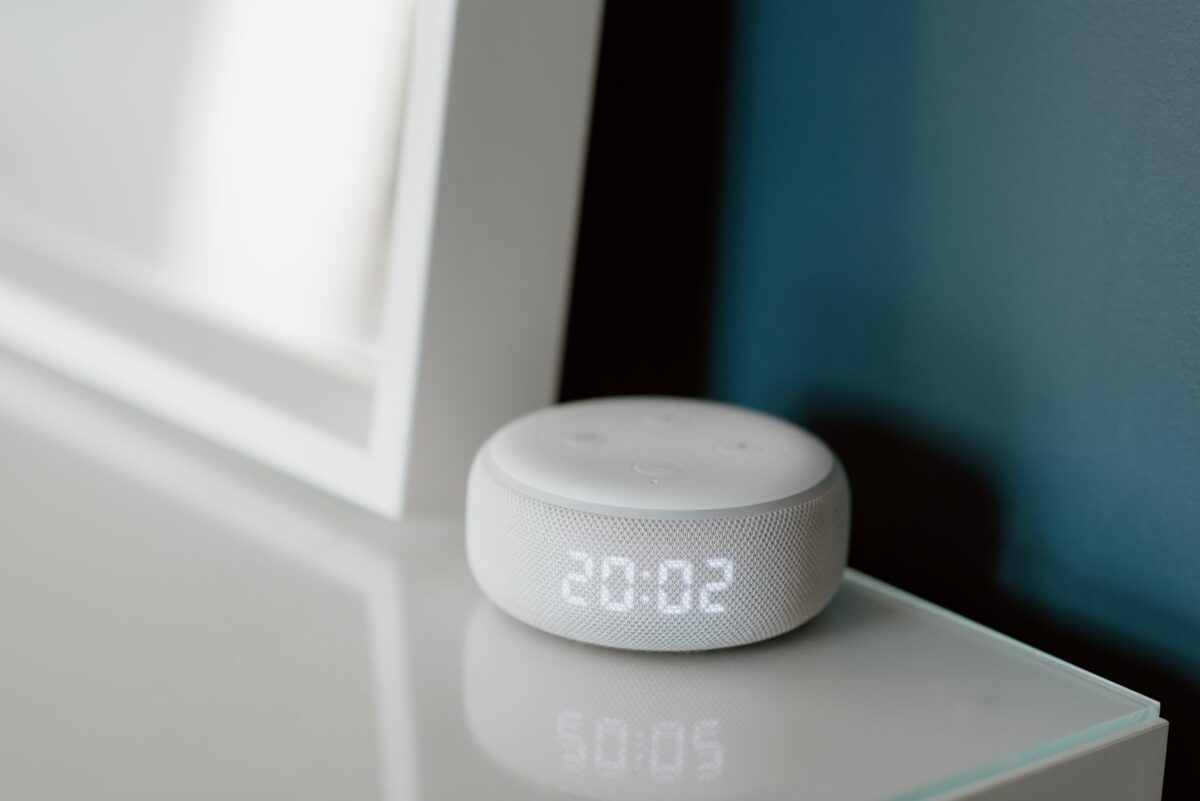 Close-up of a smart speaker with an illuminated 20:02 LED clock display on a desk.