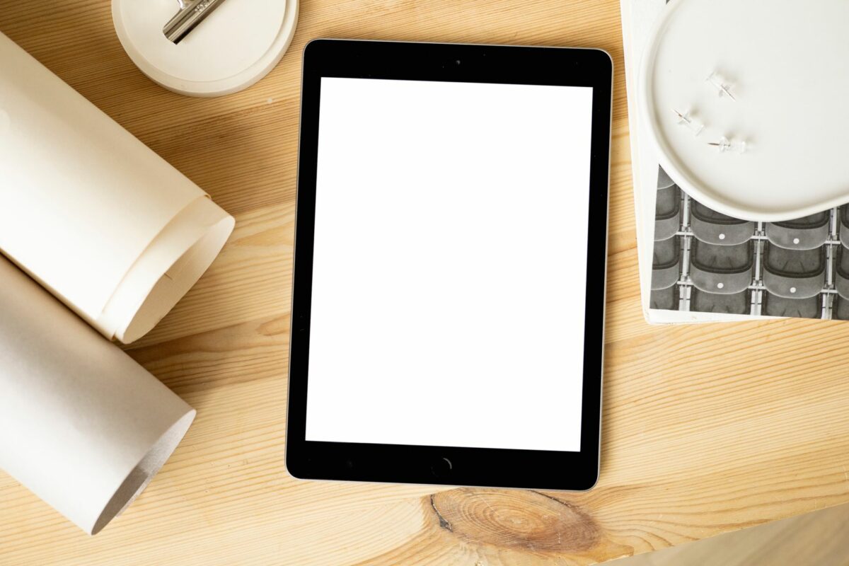 Overhead view of a tablet mockup on a wooden desk with stationery, perfect for design presentations.